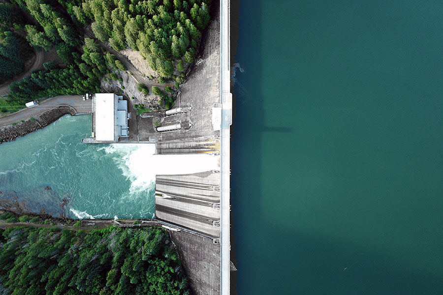Aerial photo of a dam and hydropower plant, green water and pine trees