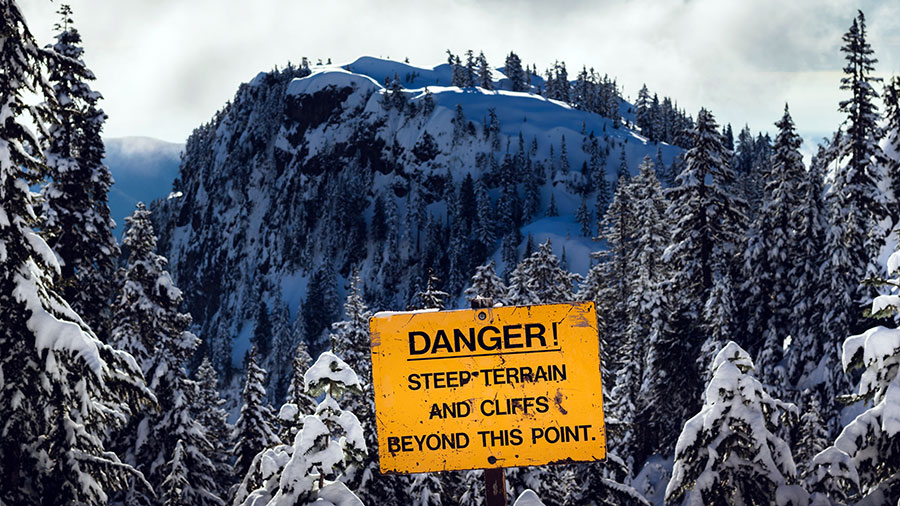 Photo of mountainous, snowy pine landscape with yellow warning sign, Vancouver, BC, Canada