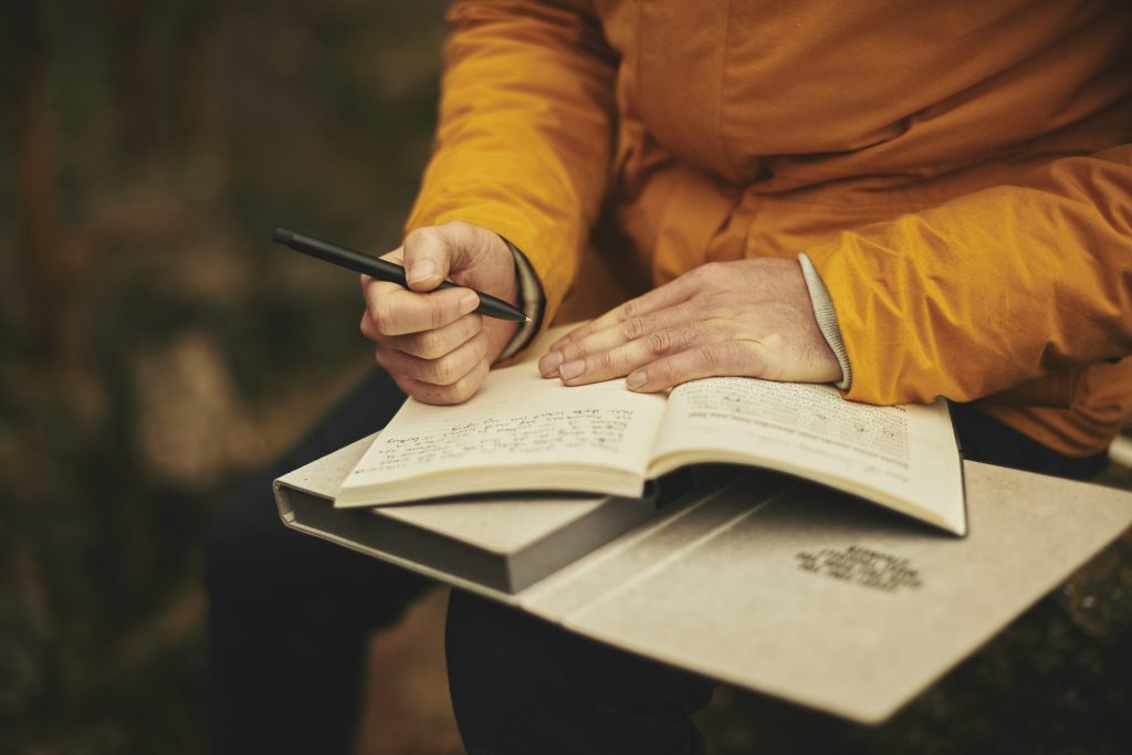 Photo of person sitting outside and writing in a journal, wearing a yellow jacket