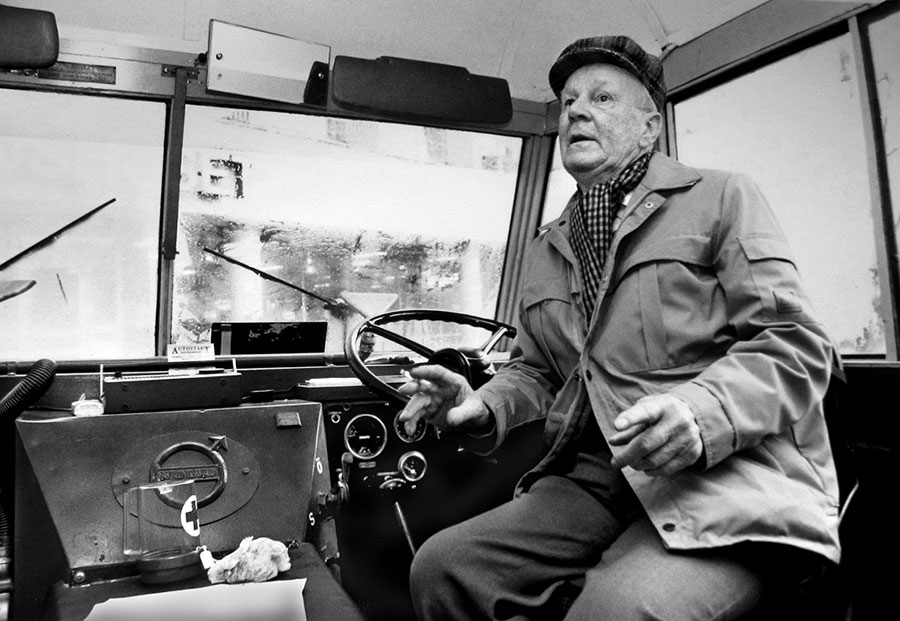 Black and white photo of an old man sitting in an old bus, one the white buses that evacuated 15 000 people from concentration camps