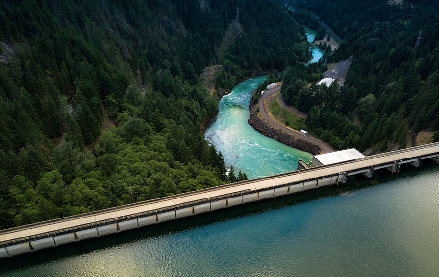 Aerial photo looking out over hydropower dam with green water and a green creek and pine forest