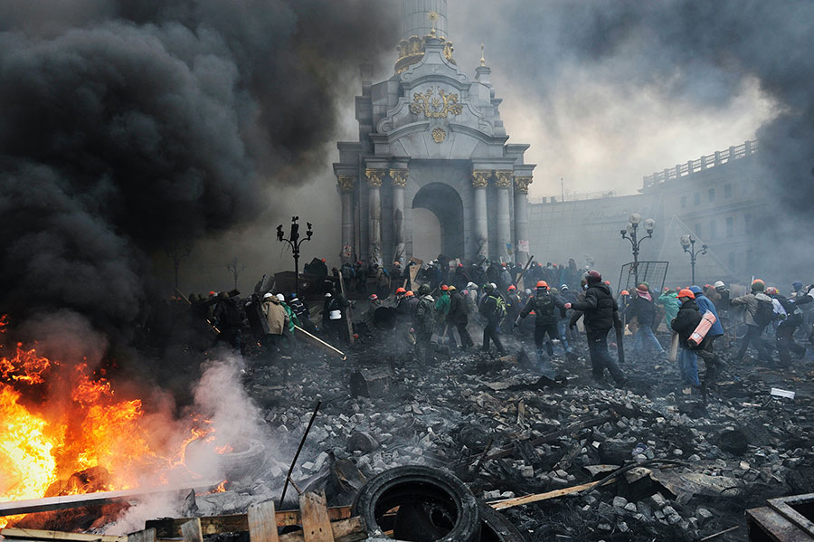 Photo of the Maidan (Independence Square), Kyiv, Ukraine with burning tires, black stone-filled ground and people with helmets during the Revolution of Dignity 2013-2014