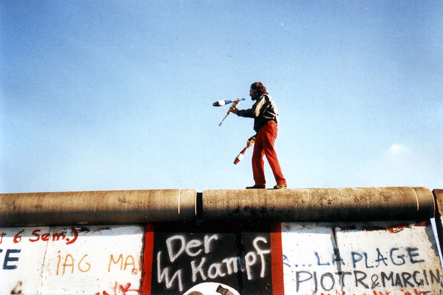 Photo of bearded man in red pants juggling on the Berlin wall