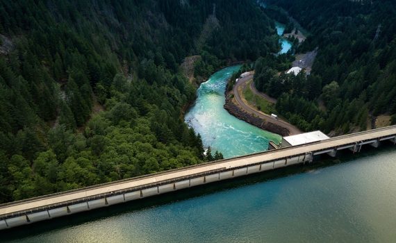 Aerial photo looking out over hydropower dam with green water and a green creek and pine forest
